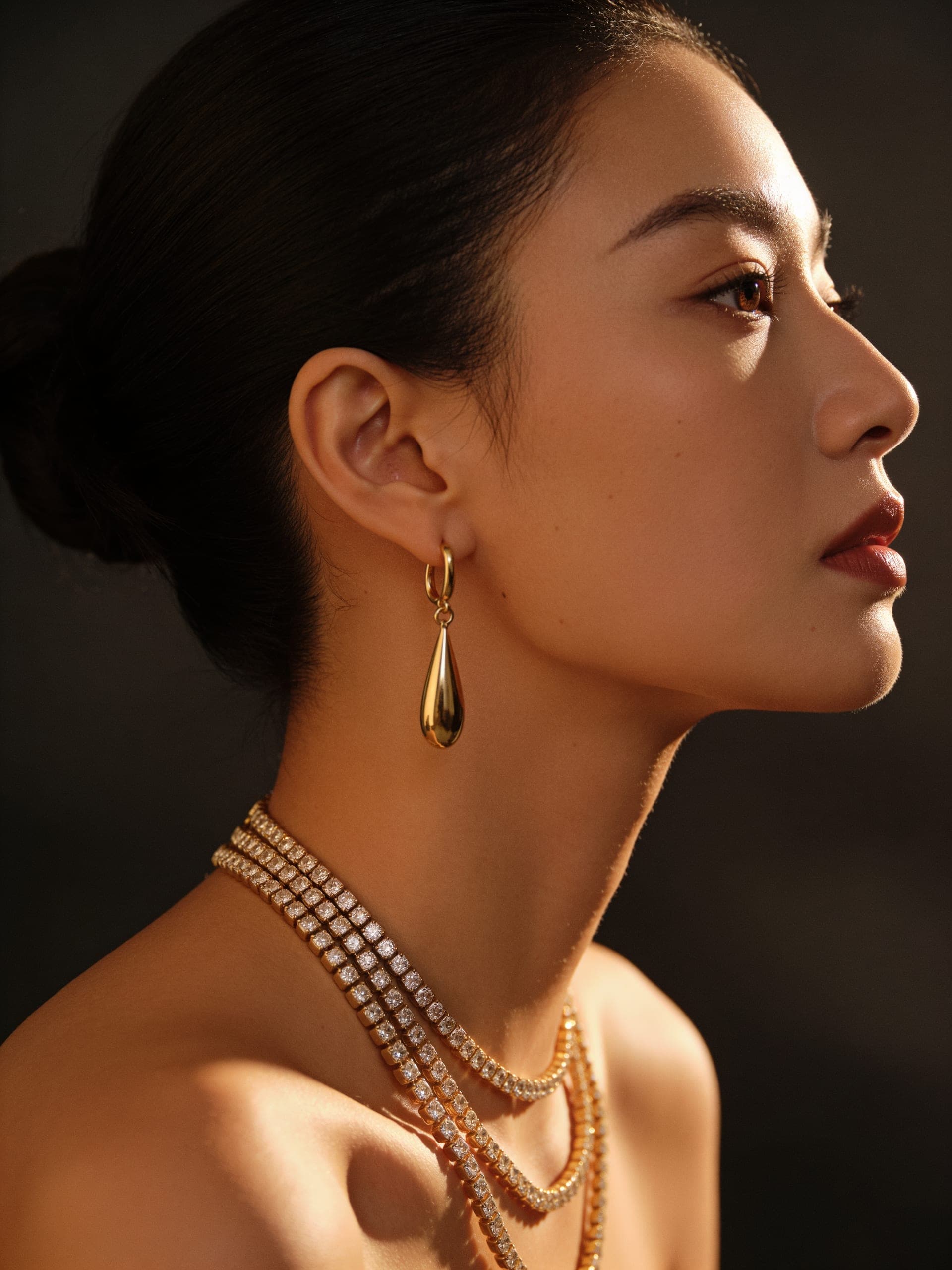 A woman in profile wearing layered Orène gold necklaces and drop earrings